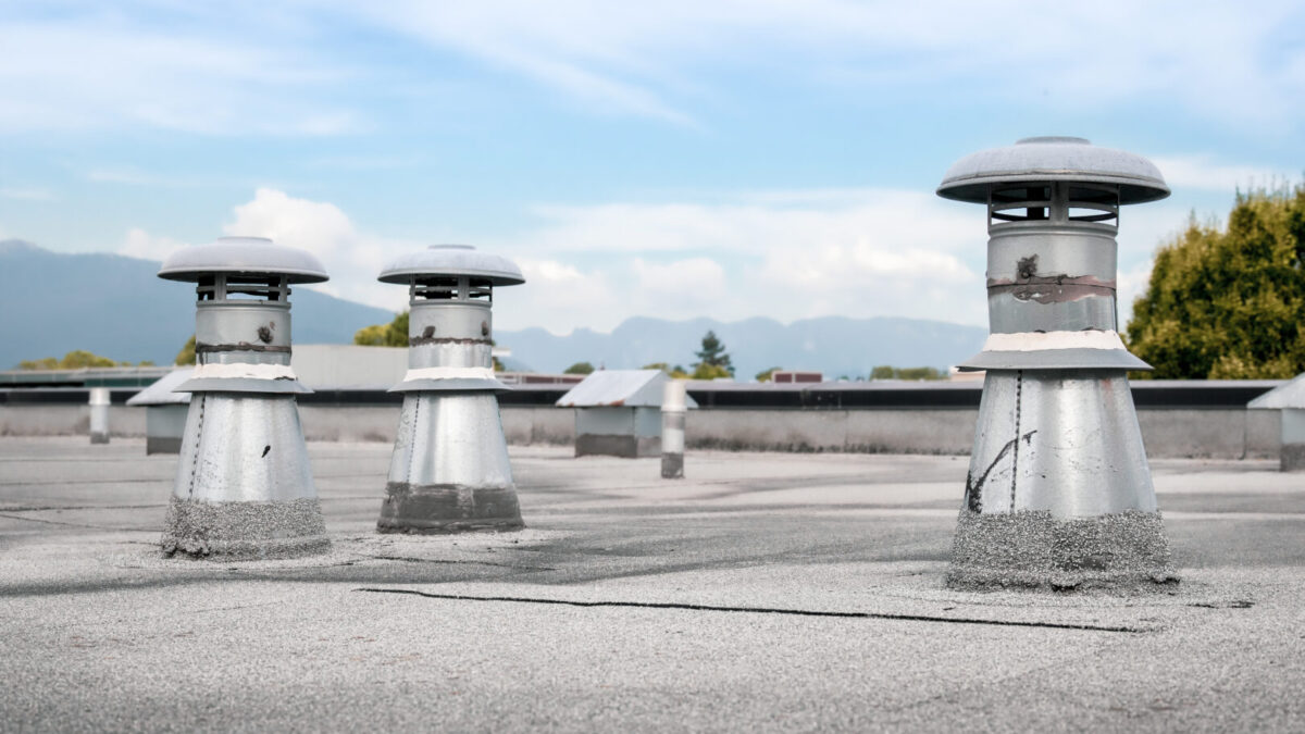 Flat roof vents on building with 2 ply SBS or modified bitumen roofing system. Group of metal ventilators such as: bathrooms and laundry exhaust and plumbing stack vent. Selective focus.